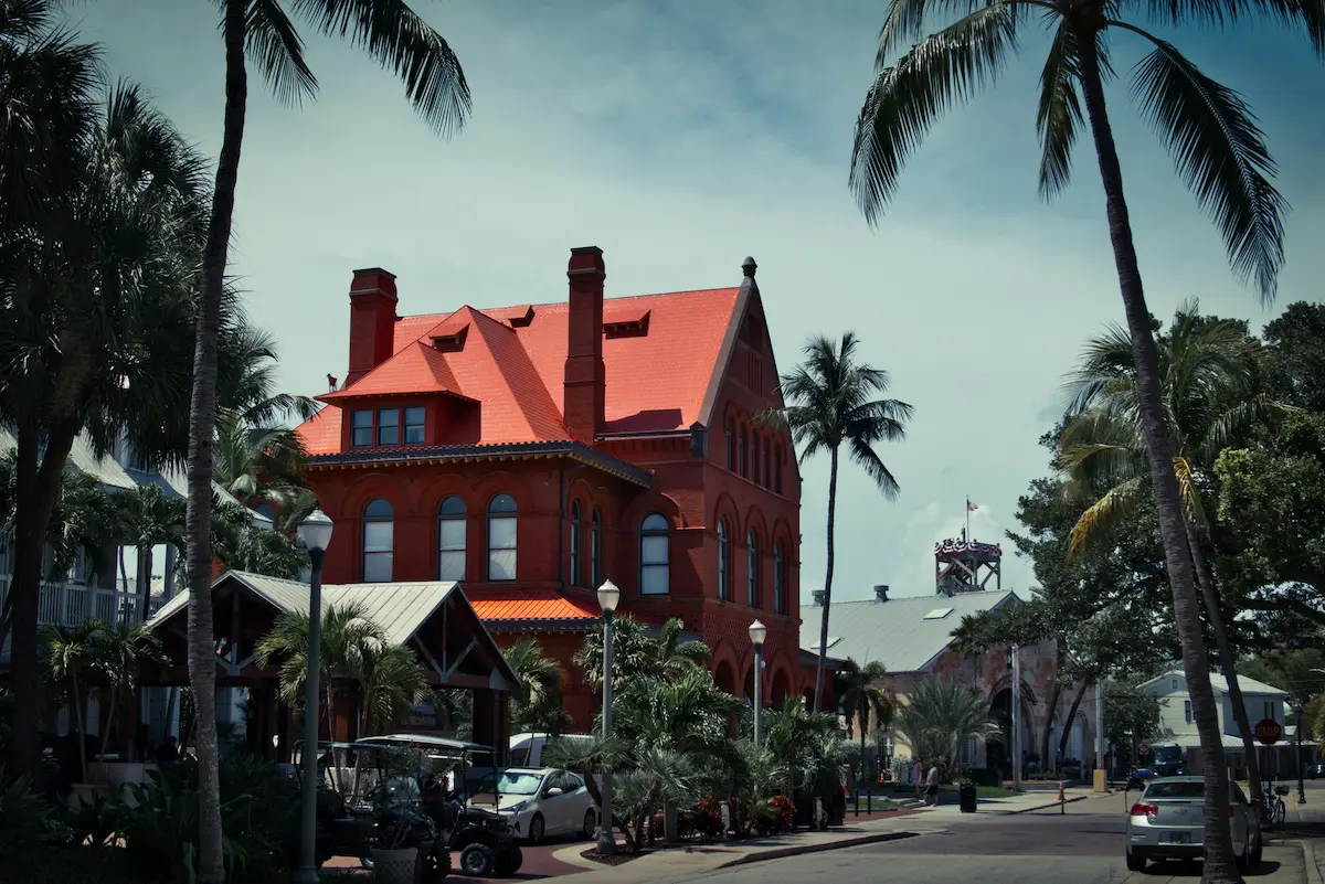 Historic red-brick building in Key West surrounded by palm trees on a sunny street