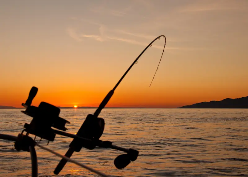 Fishing rods on a boat silhouetted against a vivid orange ocean sunset